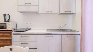 Cocina compacta con armarios blancos, un microondas, un tostador y un lavamanos.