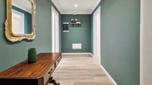Un pasillo con paredes verde azulado, un banco de madera, un espejo y una estantería con una planta.