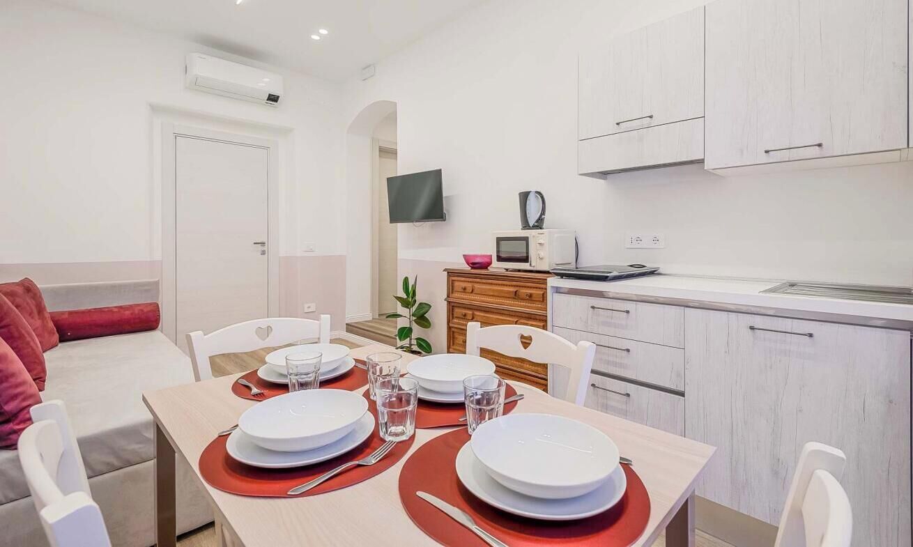 Cucina moderna con mobili bianchi, un forno a microonde e una TV montata sopra il bancone.