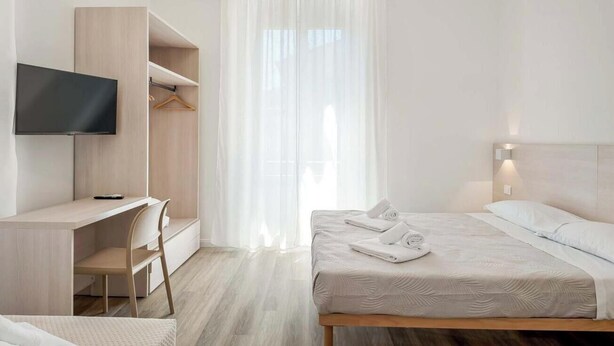 Una habitación de hotel moderna con cama, escritorio, silla, televisión y armario.