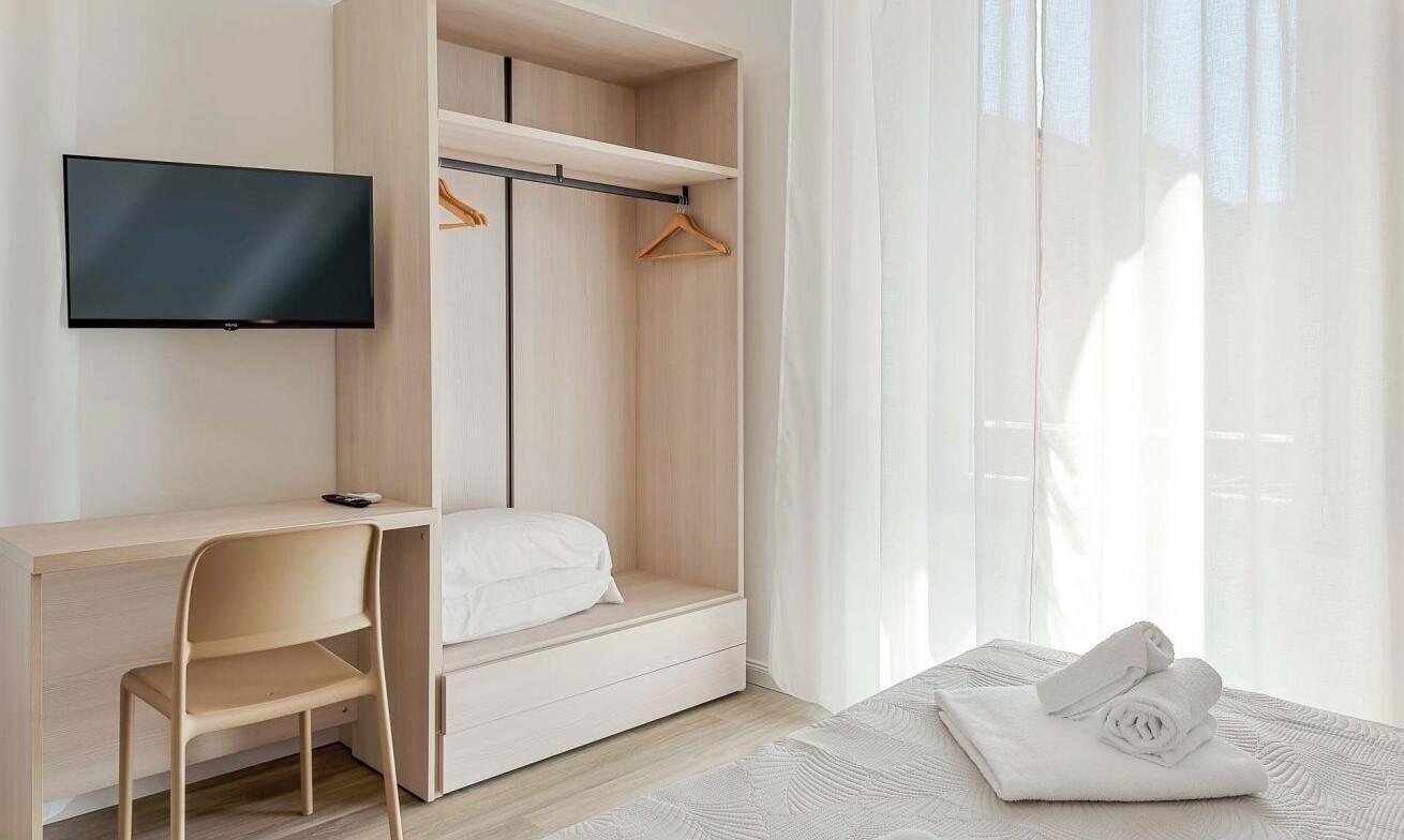 A modern bedroom with a bed, a desk, a TV, and a wardrobe.