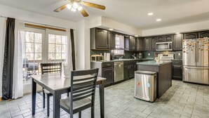Una cocina moderna con armarios oscuros, electrodomésticos de acero inoxidable y un comedor con mesa y sillas.