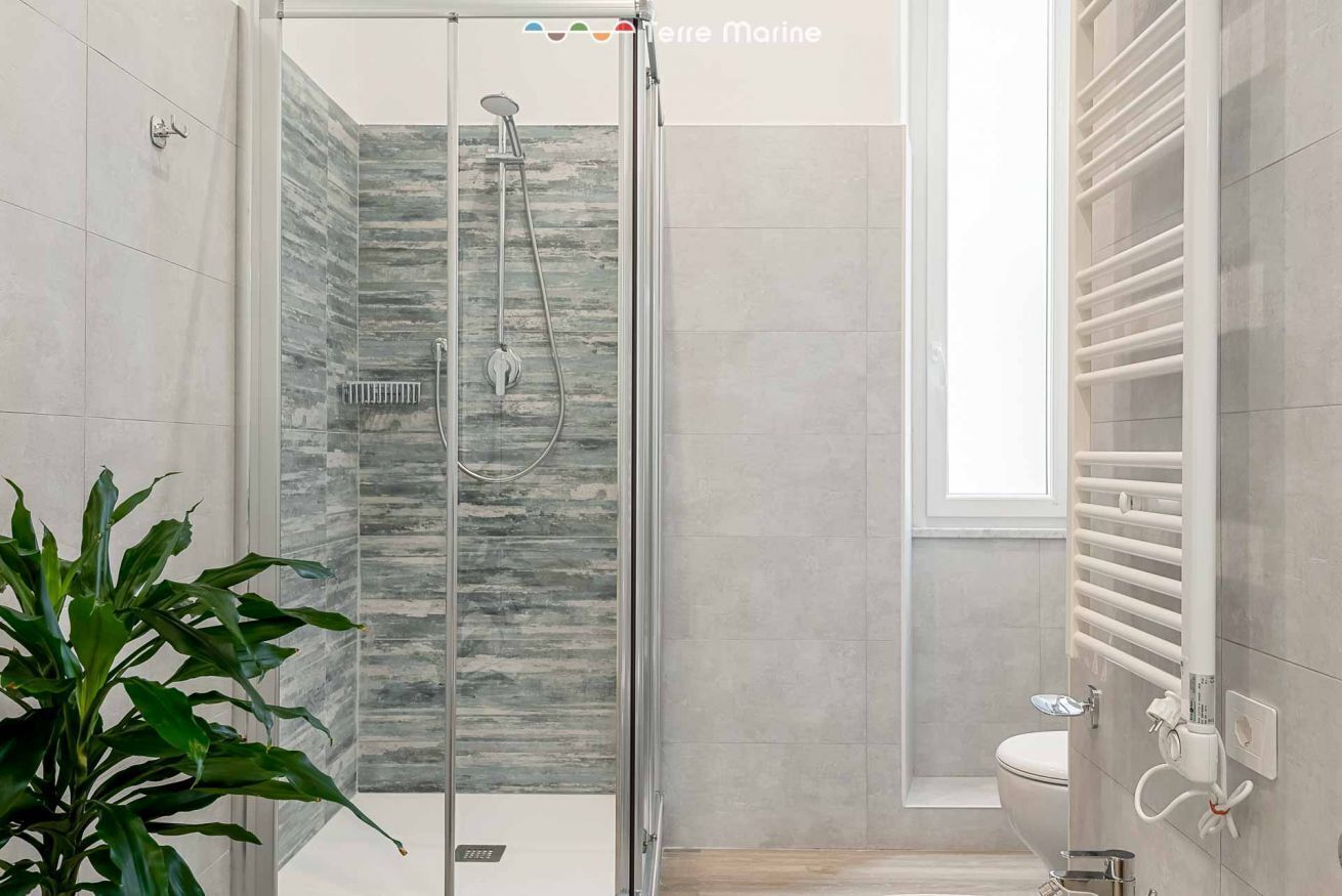 Une salle de bain moderne avec une douche à parois de verre, des toilettes blanches et un porte-serviettes intégré.