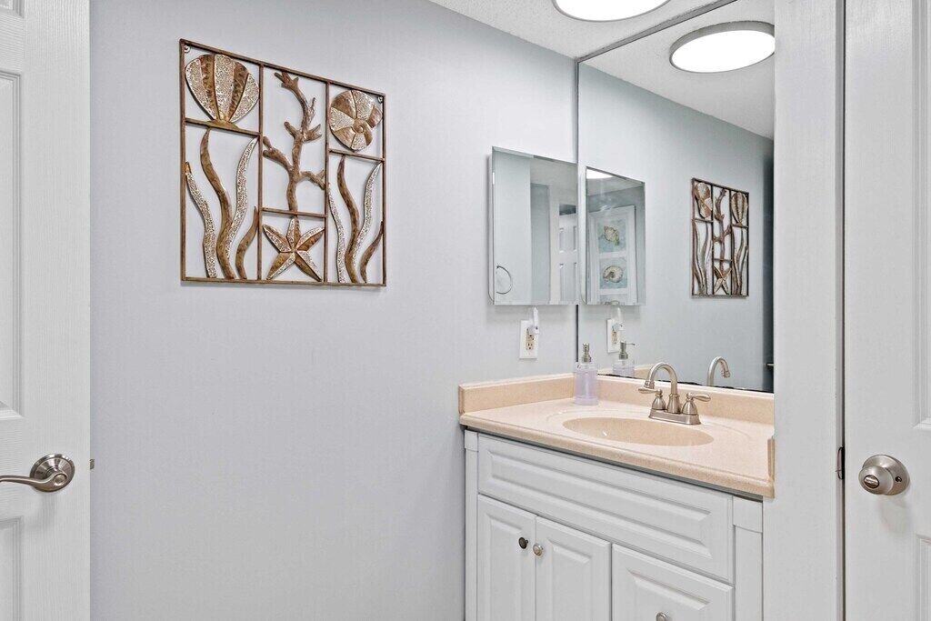Un baño con tocador blanco, lavabo color beige y un espejo grande. Se observa una obra de arte colgada en la pared sobre el lavabo.