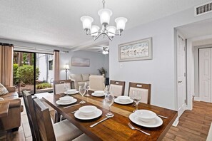 Zona pranzo con tavolo in legno apparecchiato per sei persone, un lampadario e vista sull'esterno.