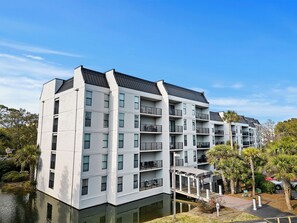 Un moderno edificio residenziale a più piani con balconi, una galleria coperta e un corpo d'acqua di fronte.