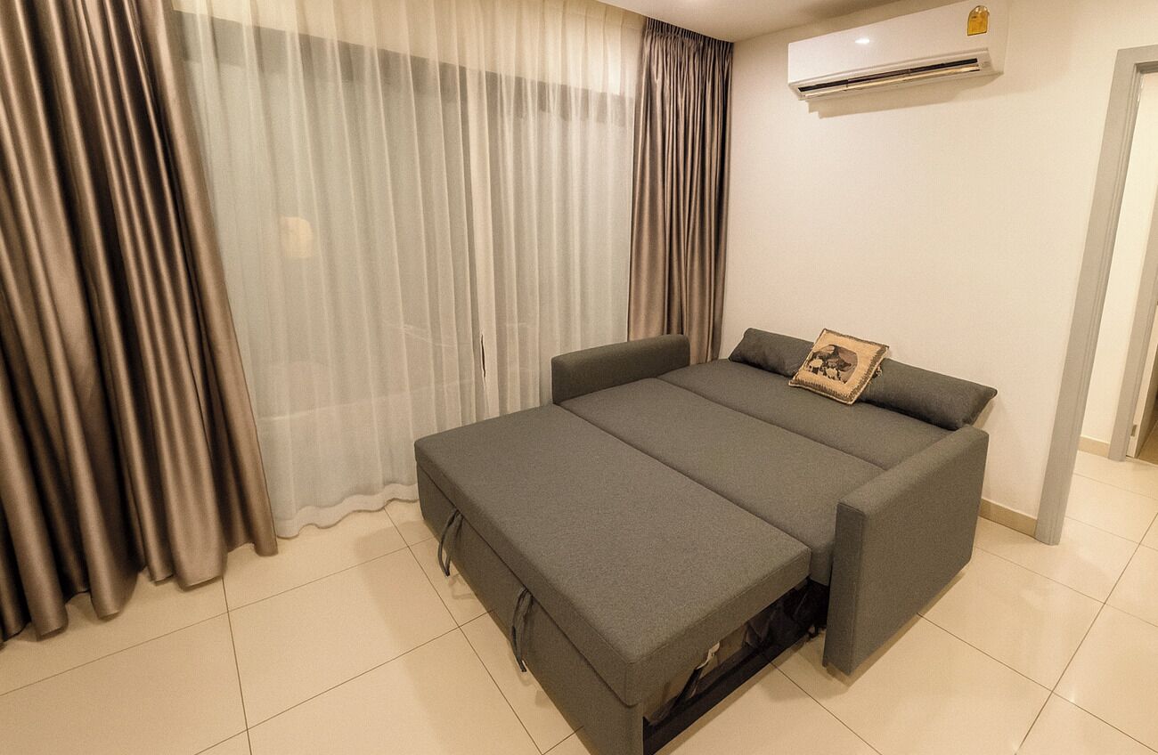 A modern bedroom with a grey sofa bed, a small bedside table, and a picture frame on the wall.