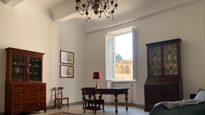 Une pièce avec un grand tapis à motifs, un meuble en bois, un bureau avec une chaise et une fenêtre donnant sur les bâtiments à l’extérieur.