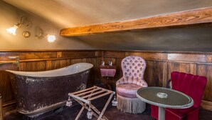Un baño de estilo antiguo con una bañera tipo pata de león, un banco de madera, un sillón tapizado y una mesita.