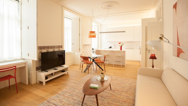 A modern living room with a flat-screen TV, a sofa, a coffee table, and a dining area with chairs and a table. - FLH Downtown Central Minimalist Apartment (Lisboa ciudad)