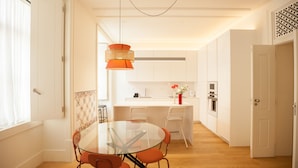 A modern kitchen with white cabinets, a central island, and a hanging orange pendant light. - FLH Downtown Central Minimalist Apartment (Lisboa ciudad)