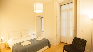 A bedroom with a bed, bedside lamps, a chair, and a door leading to another room. - FLH Downtown Central Minimalist Apartment (Lisboa ciudad)