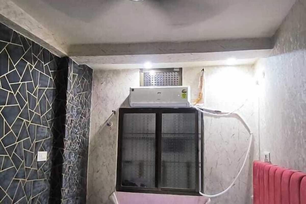 A bedroom with a bed, a ceiling fan, a window with an air conditioning unit, and a decorative wall on one side.