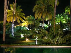 Ein tropisches Resort bei Nacht, mit Palmen und einem Pool.