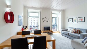 A modern living room with a dining area, a grey sofa, a TV on a stand, and large windows with a city view. - The Restauradores Collection - Majestic (Lisboa)
