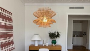 A dining area with a wooden table, white chairs, a woven pendant light, a vase with green foliage, and a striped towel on the wall. - The Restauradores Collection - Majestic (Lisboa)