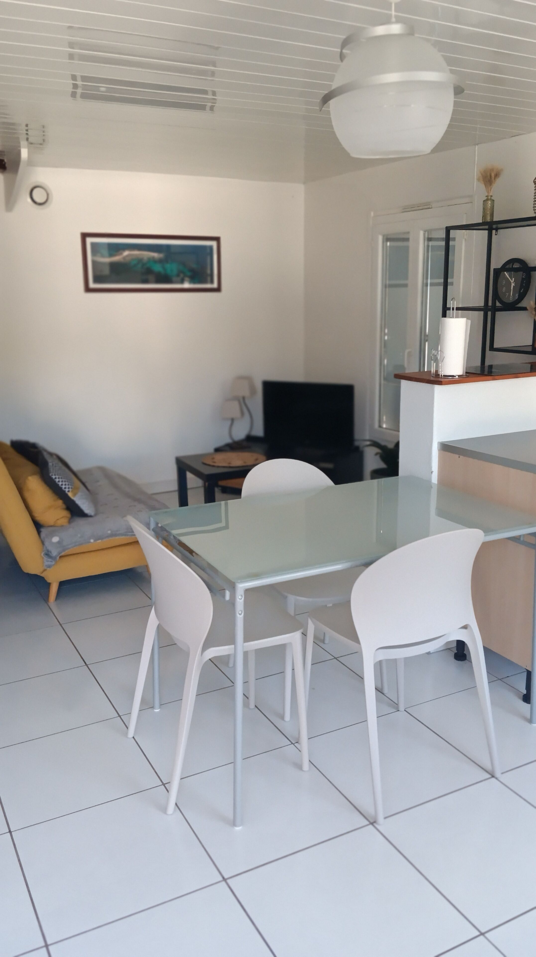 Una sala moderna con una mesa de vidrio, sillas blancas, un sofá, un televisor y un cuadro en la pared.