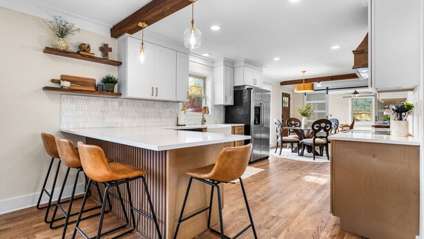 Een moderne keuken met een centraal eiland, barkrukken, houten balken en hanglampen.