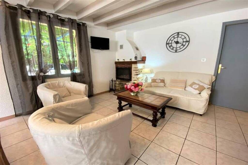 Un salon avec un canapé, un fauteuil et une table basse ornée de fleurs. On y trouve également une cheminée et une horloge au mur.