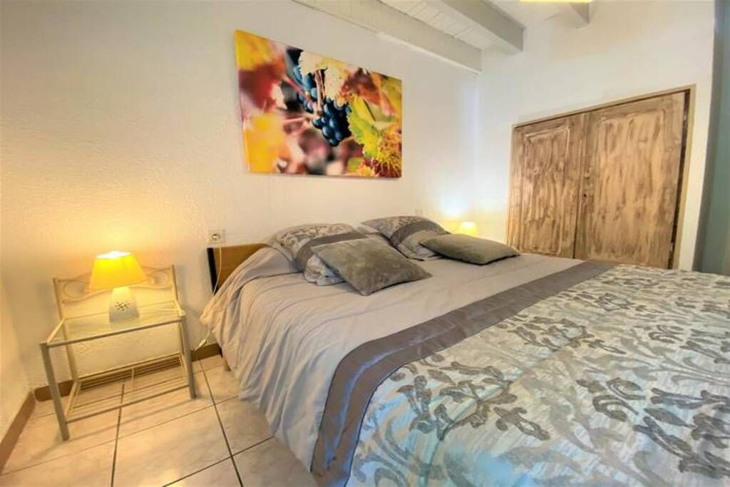 Een slaapkamer met een bed, nachtkastje, lamp, houten garderobe en een kleurrijk abstract schilderij aan de muur.