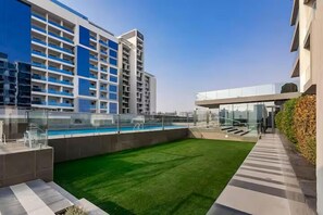 A rooftop pool with a glass railing, a green lawn, and a modern building with multiple balconies.