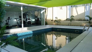 A swimming pool with a glass enclosure, a fitness area with exercise equipment, and a white fence. - One Bedroom Luxury apartment in Maitama, Abuja (Abuja)