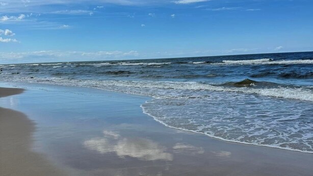 Una spiaggia con onde, cielo sereno e nuvole.