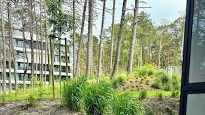 Un patio con sedie in vimini e un tavolo, circondato da vegetazione e un edificio sullo sfondo.
