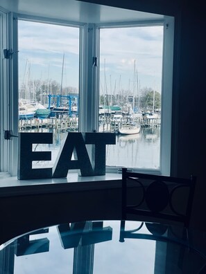 A view of a marina with boats docked, a large window with the word "EAT" in the foreground, and a chair in the foreground.