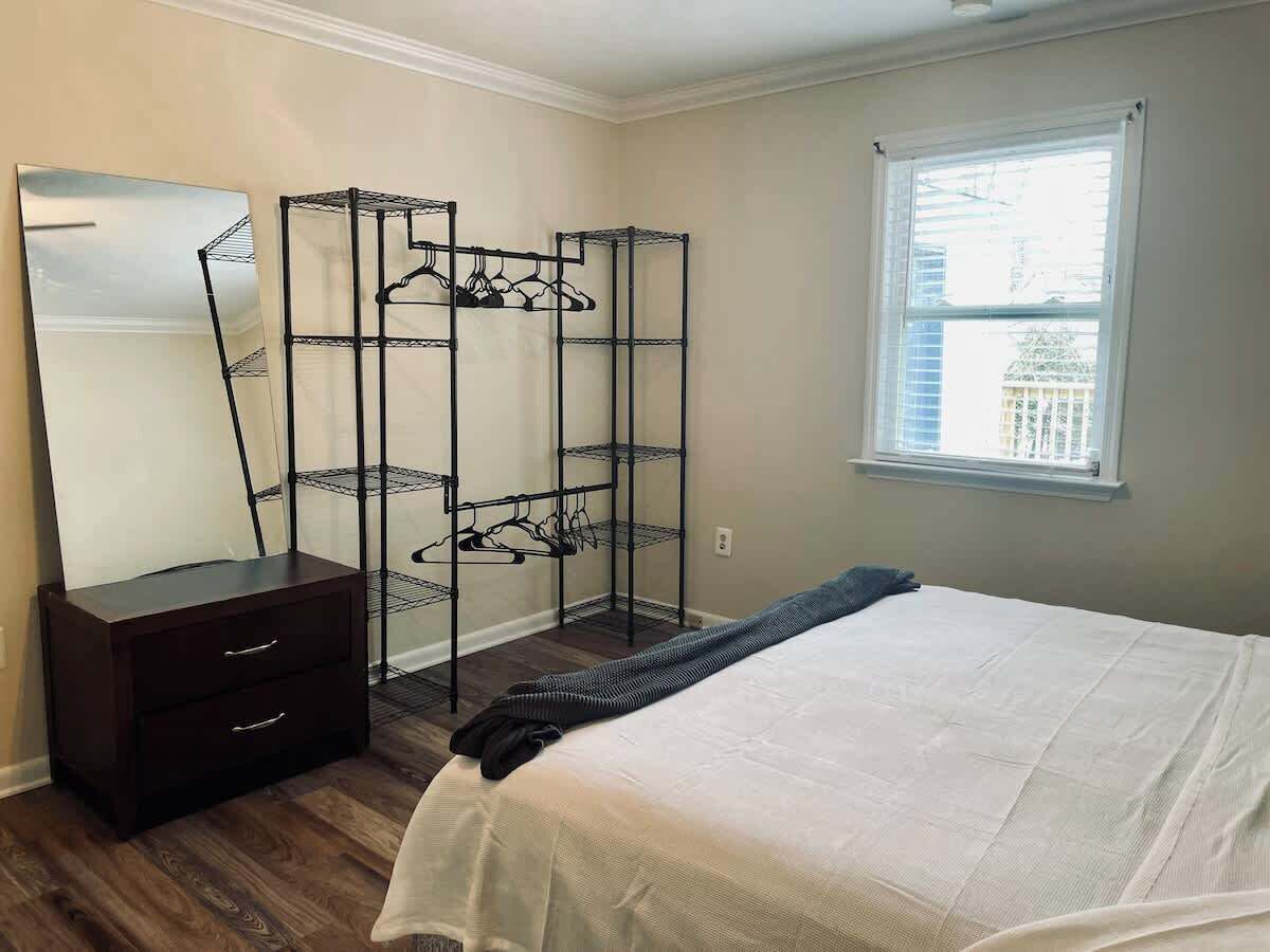 Een slaapkamer met een bed, een kaptafel, een spiegel en een metalen kledingkast met planken.