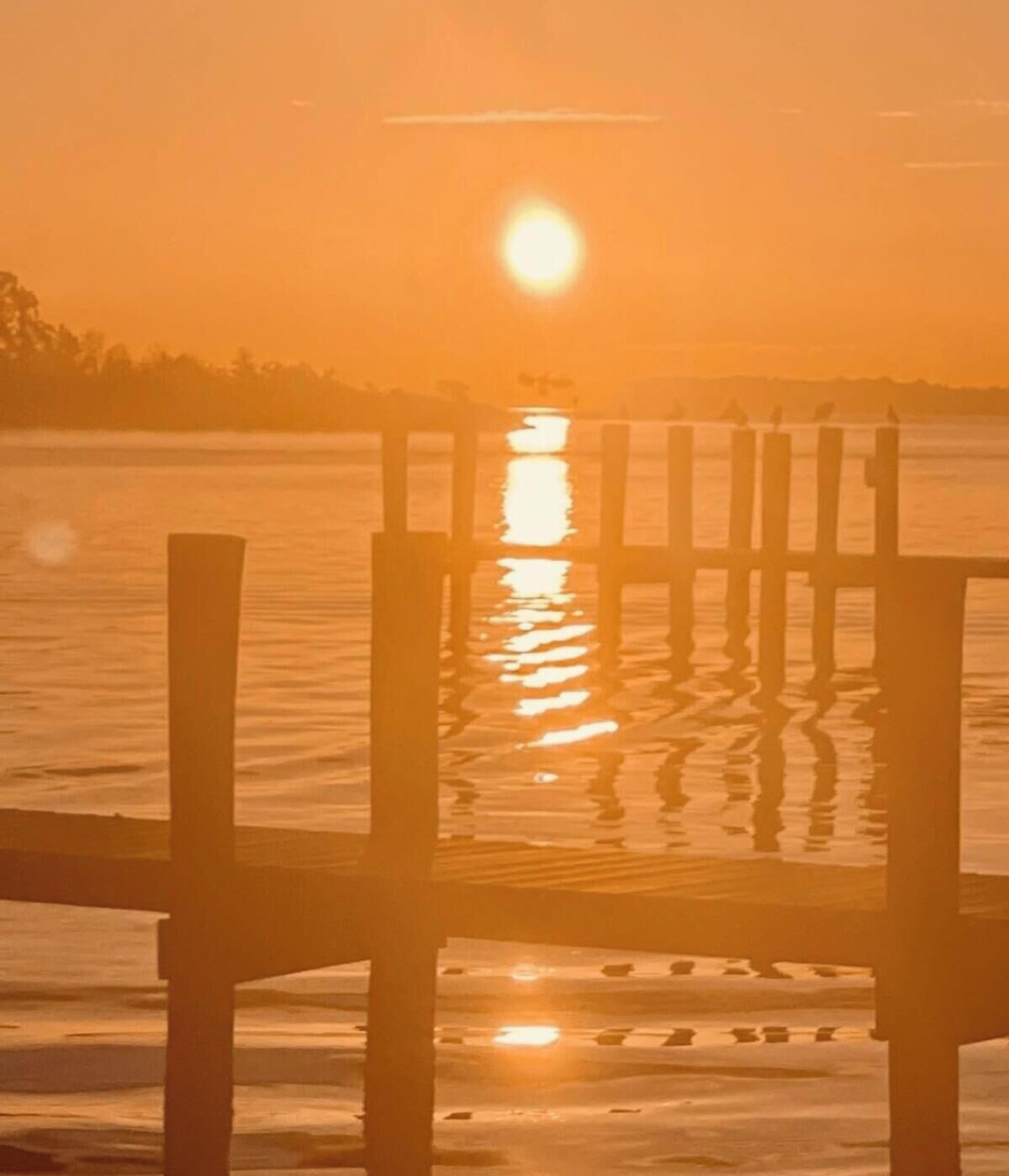 Eine Holzsteganlage, die sich in ein Gewässer erstreckt, mit einem Sonnenuntergang im Hintergrund.