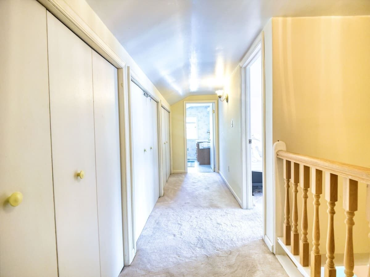 A narrow hallway with white doors, a wooden staircase, and a carpeted floor.