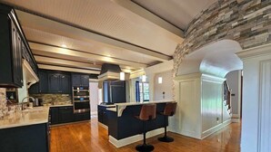 A spacious kitchen with dark cabinetry, a central island, and two bar stools. - Creekside Haven With Dock Scenic Views (Hollywood)