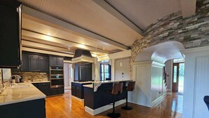 A modern kitchen with dark cabinetry, a central island, and a stone accent wall. - Creekside Haven With Dock Scenic Views (Hollywood)