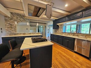 A modern kitchen with a central island, dark cabinetry, and a stone backsplash. - Creekside Haven With Dock Scenic Views (Hollywood)