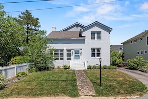 A two-story house with a stone pathway leading to the front door, surrounded by a white picket fence and greenery. - Solomons Island 6BR Family Getaway (Solomons)