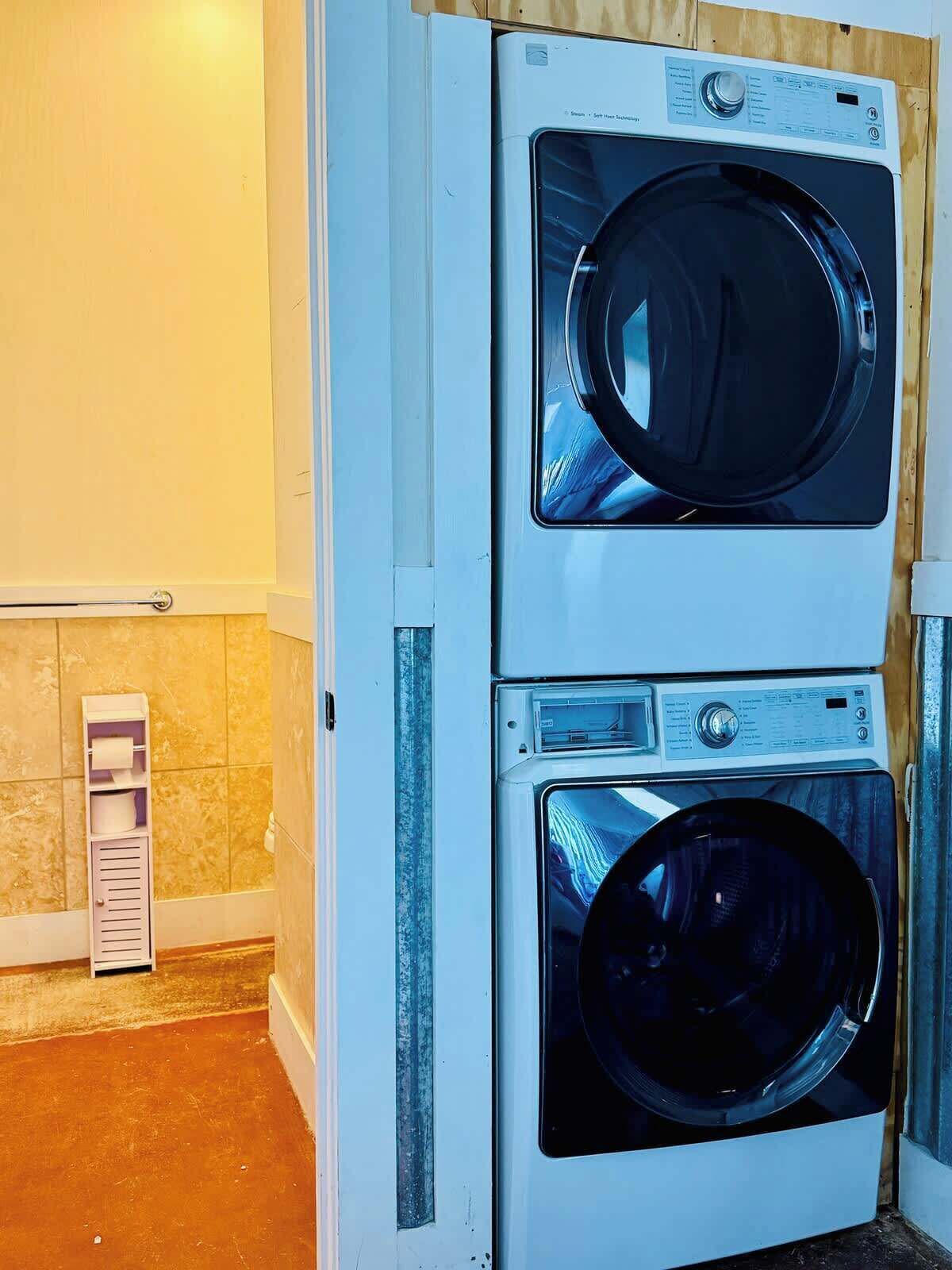 A wall-mounted washer and dryer unit in a laundry room with tiled walls and a wooden floor.