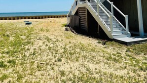 A beachfront house with a staircase leading to a balcony, a sandy beach in the background, and a clear blue sky. - 4-bedroom Luxury Private Beach Getaway (Scotland)