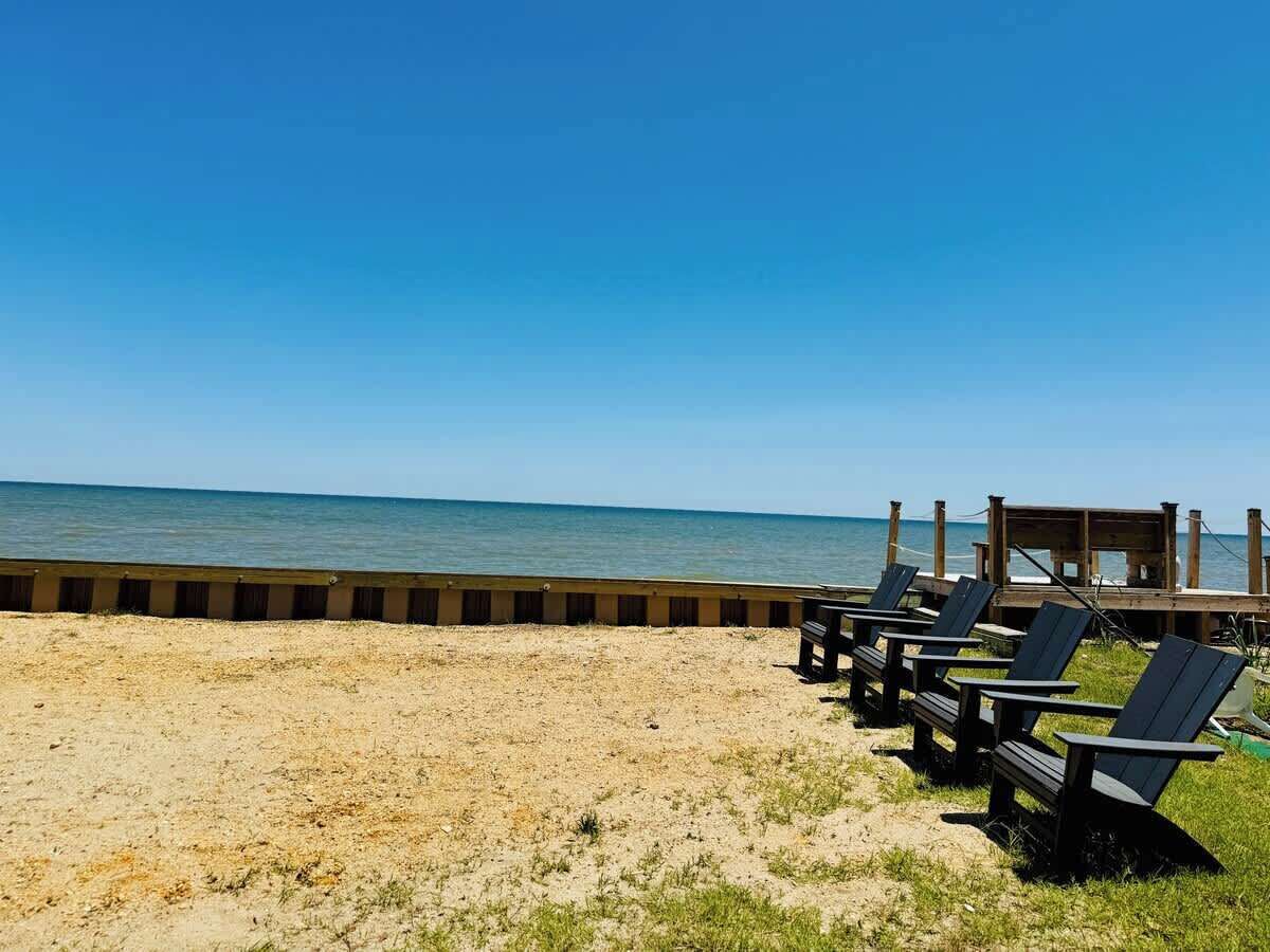 A beach with a wooden deck and lounge chairs facing the ocean.