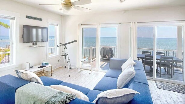 A spacious living room with a large sofa, a telescope, and a balcony with a view of the sea. - 4-bedroom Luxury Private Beach Getaway (Scotland)