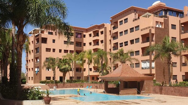 Um hotel com vários andares, piscina, palmeiras e um gazebo coberto.