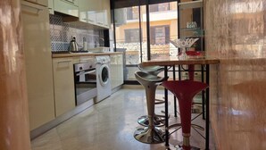 Cozinha compacta com máquina de lavar, pia e um banquinho.