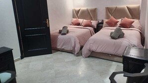 Quarto com duas camas, uma porta preta, uma mesinha e ar-condicionado fixado na parede.