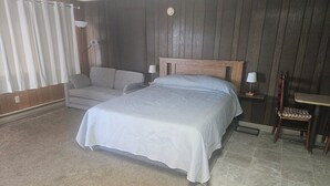 Une chambre à coucher avec un lit, un canapé, une chaise, une lampe et une petite table.