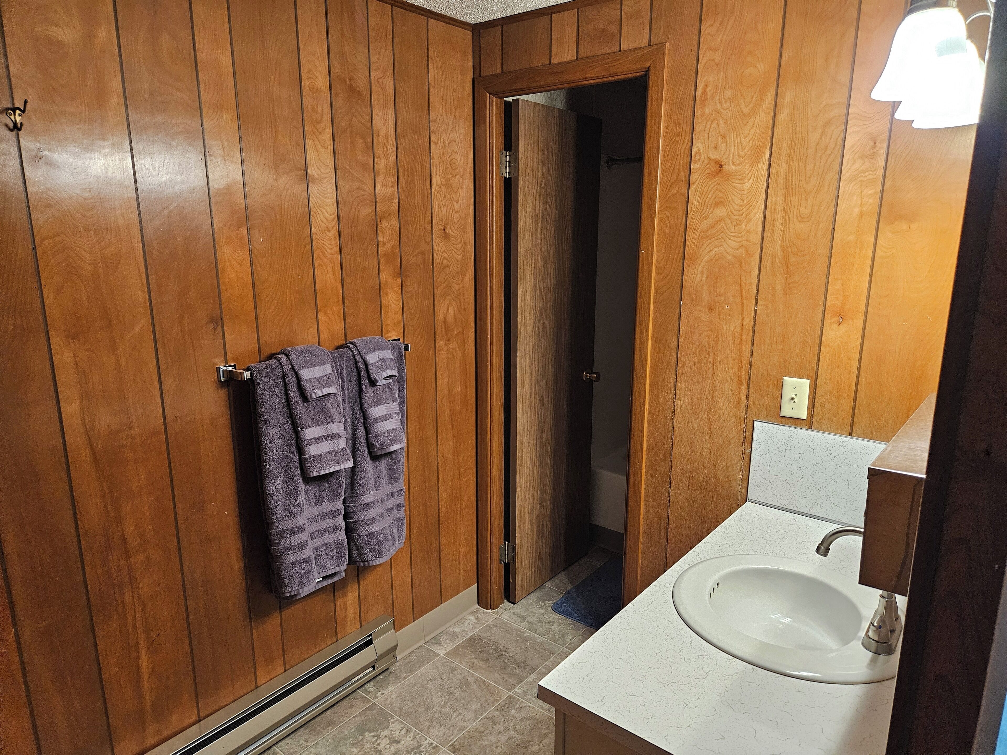 A bathroom with wooden panel walls, a white sink, and two towels hanging on a towel rack.