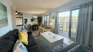 A modern living room with a sofa set, a dining table, and a balcony with a view of buildings. - Myrtle Beach Resort B0423 (Myrtle Beach)