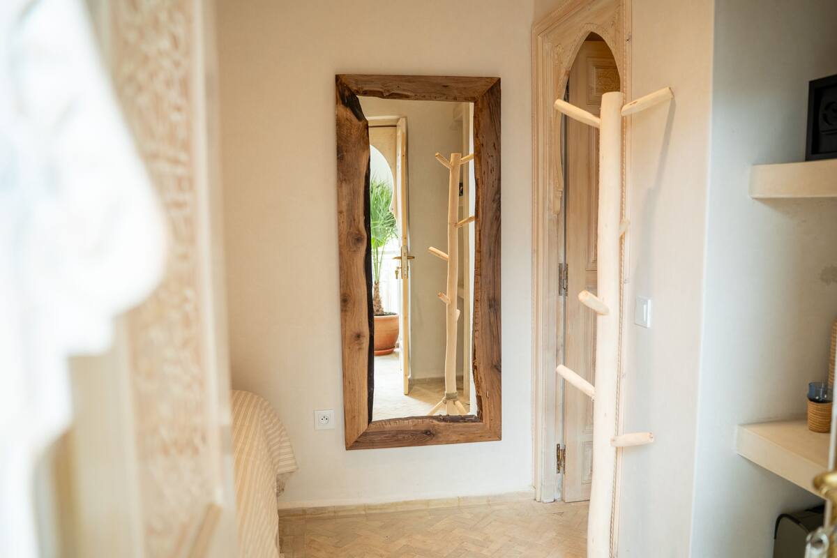 A narrow hallway with a large mirror on the wall, a wooden door frame, and a small shelf with a basket.