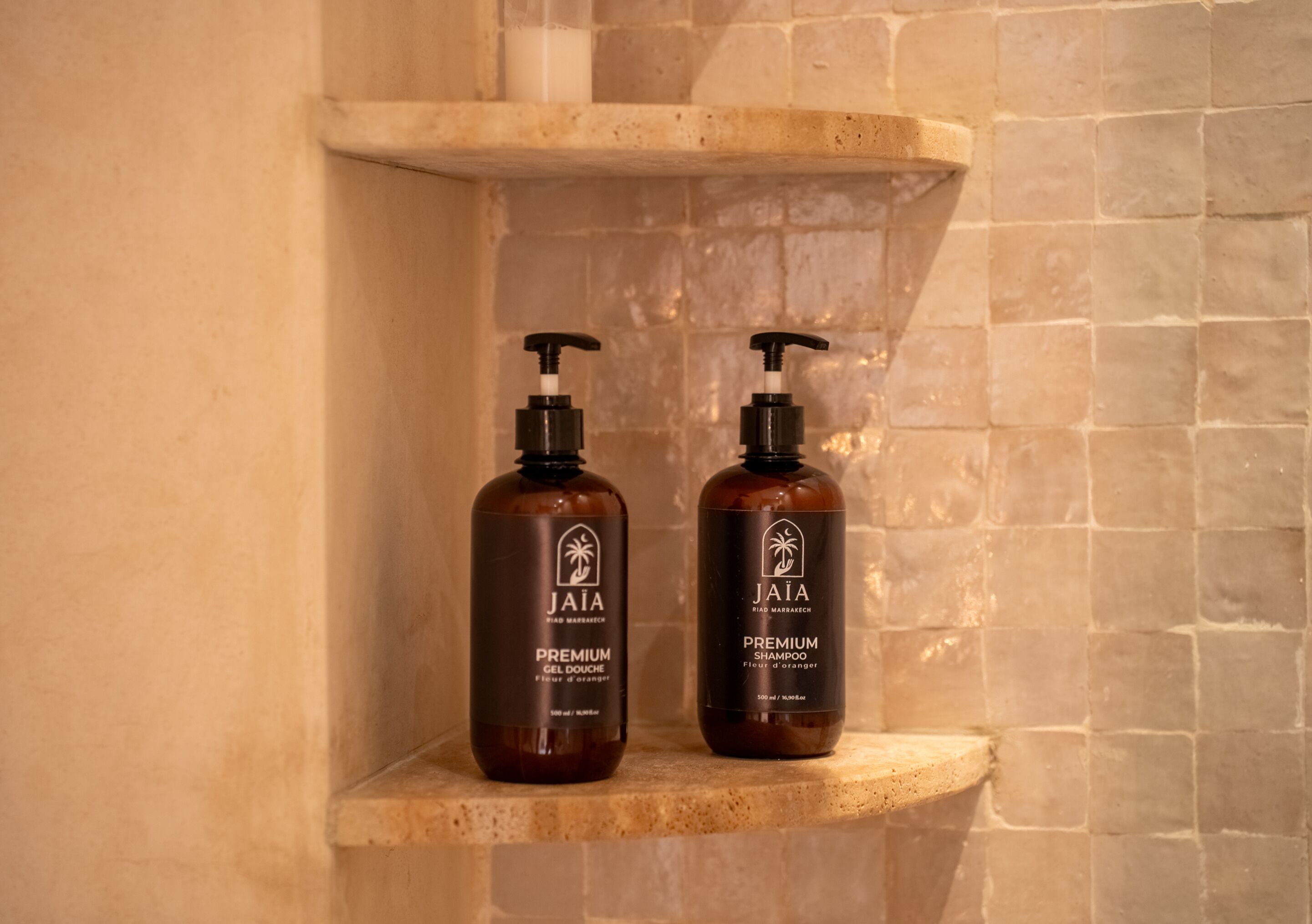 Two bottles of Jaia Premium Gel Douche on a shelf in a bathroom with a stone wall.