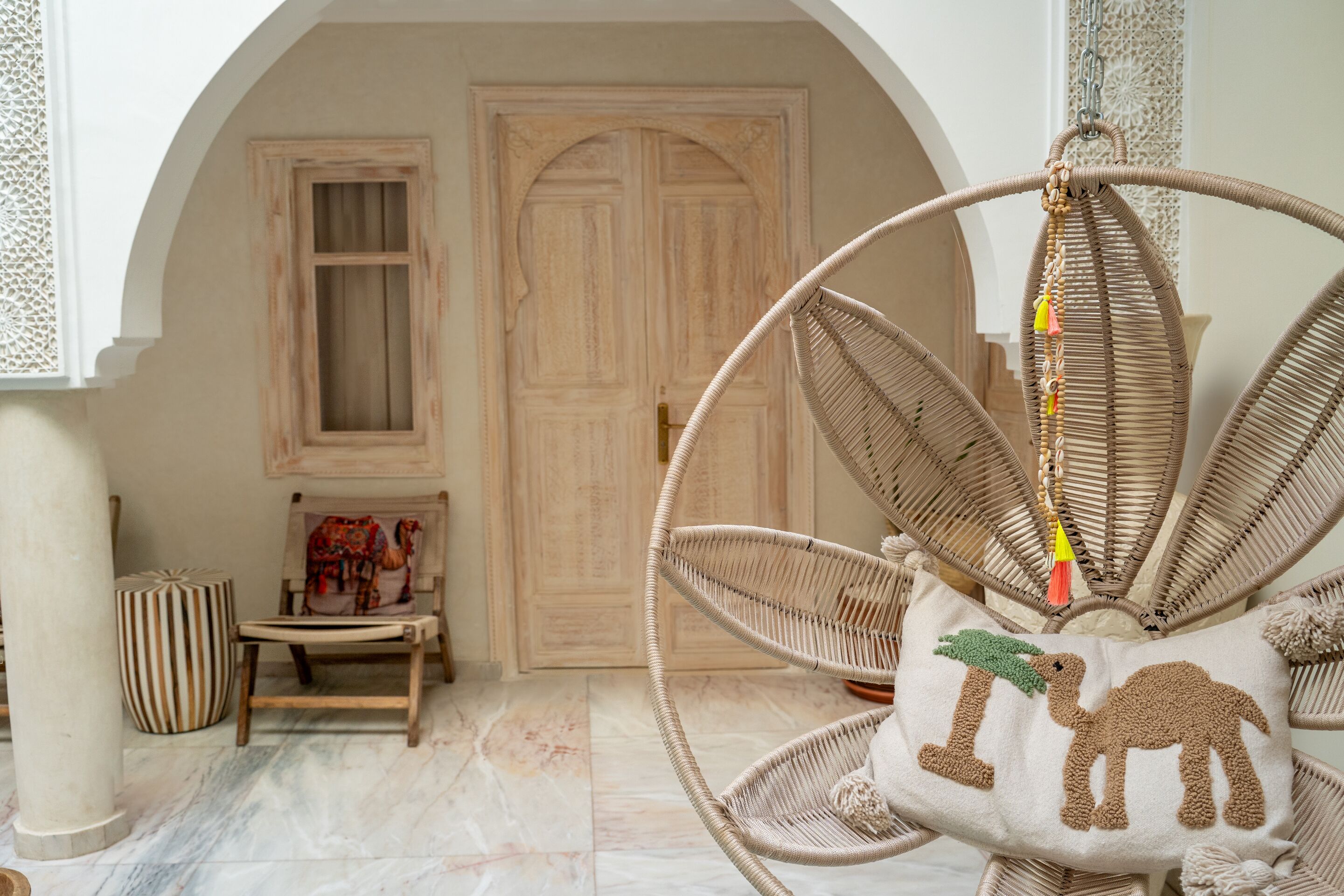 A wicker chair with a cushion featuring a camel design, a wooden door, and a striped ottoman.
