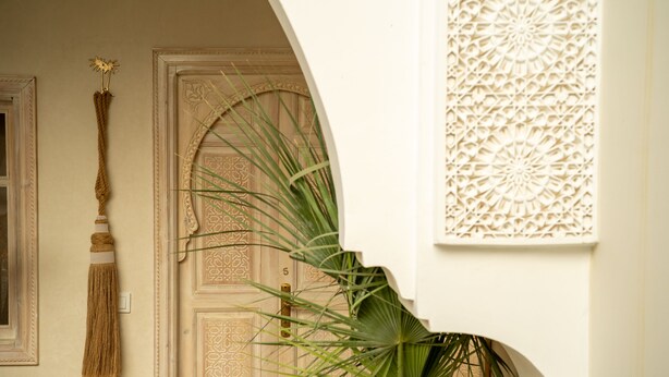 A hallway with a wooden door, a wall-mounted tassel, and a large plant. - Riad Jaia (Marrakech)